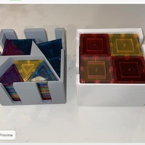May include: A gray plastic storage bin containing translucent blue, purple, and yellow triangular magnetic tiles, positioned next to a white plastic storage bin containing translucent red and yellow square magnetic tiles.
