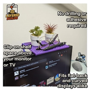 May include: A purple plastic clip-on shelf mounted on top of a computer monitor. The shelf holds two small potted artificial plants, a pair of black-rimmed eyeglasses, and a black pen. Text on the image reads: Layered Builds, No drilling or adhesive required, Clip-on shelf space above your monitor or TV, Fits flat-back and curved displays alike.