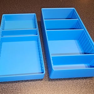 May include: Two bright blue rectangular storage organizers with internal dividers. Each tray features vertical grooves along the interior side walls, allowing for adjustable compartment spacing to suit various storage needs.