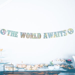 May include: A map-themed banner with the words "The World Awaits" in large letters. The banner is strung up on a white wall, and there is a table with food and drinks in the foreground.