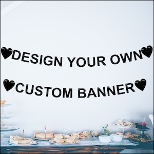 May include: Black banner with the text "DESIGN YOUR OWN" and "CUSTOM BANNER" strung across a white wall. Black heart shapes are at each end of the banner. A table with food is in the foreground.