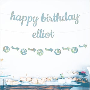 May include: A blue and white map themed birthday banner with the text "happy birthday elliot". The banner is strung with small paper airplanes and globes.