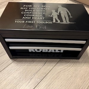 May include: Black toolbox with two drawers and silver handles. The top of the toolbox has an engraved message and a silhouette of a father and child. The text on the toolbox reads "KOBALT".