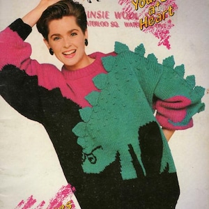 Könnte beinhalten: Ein Cover für ein Vintage-Pullovermuster mit einer Frau in einem schwarzen, rosa und grünen Pullover im Dinosaurier-Design. Das Cover enthält den Text "Young at Heart" und "Jeunes de Coeur".