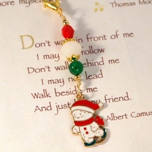 May include: A gold-tone lobster clasp charm featuring a red faceted bead, a white round bead, and a green round bead, finished with a dangling enamel snowman charm wearing a red hat and scarf while ice skating on blue skates.