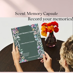 Puede incluir: Una persona sostiene un libro verde oscuro titulado "Scent Memory Capsule" con detalles florales. El texto del libro dice "A Shared Sensory Keepsake". Un jarrón con flores naranjas y rojas está cerca. El texto "Record your memories!" está encima del libro.