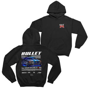 Puede incluir: Sudadera con capucha negra con un gráfico de un coche Nissan Skyline GT-R R34 azul y plateado y la palabra "BULLET". La parte delantera de la sudadera tiene un pequeño logotipo GT-R rojo y blanco.