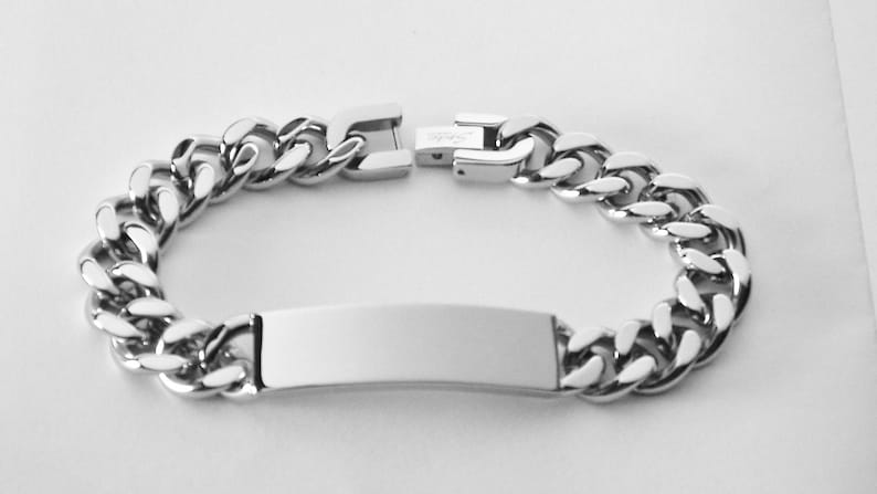 May include: A silver chain bracelet with a rectangular tag. The bracelet is made of a thick, curb chain style.