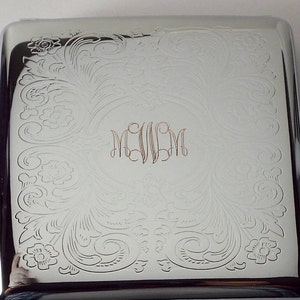 May include: Silver cigarette case with an engraved floral design and the monogram "EVM" in the center.