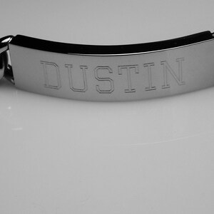 May include: A silver chain bracelet with a rectangular tag engraved with the name "DUSTIN".