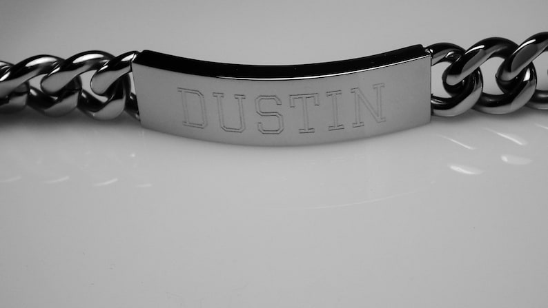 May include: A silver chain bracelet with a rectangular tag engraved with the name "DUSTIN".