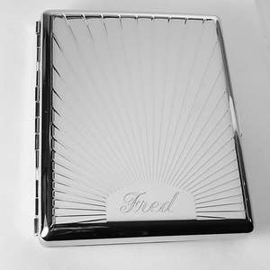 May include: A silver cigarette case with a sunburst design and the name "Fred" engraved on the front.