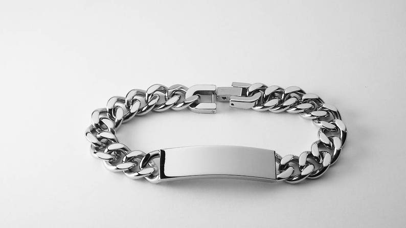May include: A silver chain bracelet with a blank rectangular tag. The chain is a curb style.