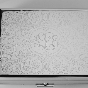 May include: A silver cigarette case with an engraved floral design and monogrammed initials.