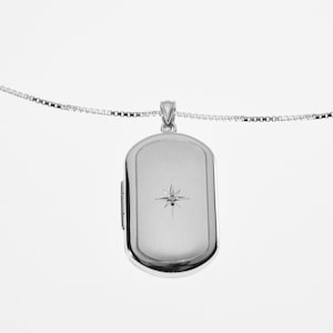 May include: A silver locket necklace with a small diamond in the center. The locket is rectangular and has a smooth, polished finish.