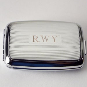 May include: A silver rectangular cigarette case with a ribbed design and the initials "R.W.Y." engraved on the front.