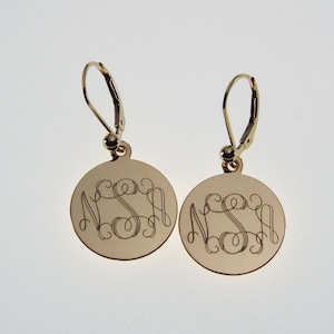 May include: Gold-toned earrings with a round disc featuring the monogram "NSA" in a cursive script.