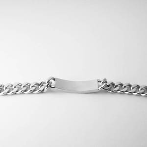 May include: A silver chain bracelet with a blank rectangular tag. The chain is a curb style.