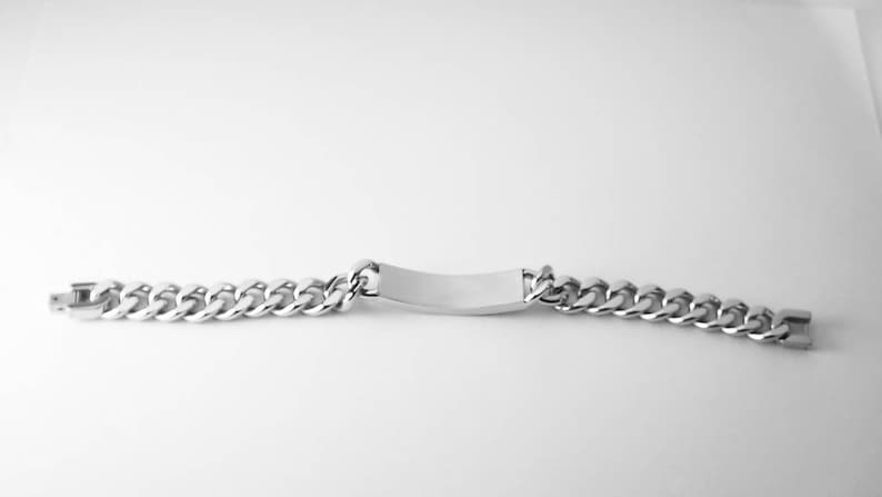 May include: A silver chain bracelet with a blank rectangular tag. The chain is a curb style.