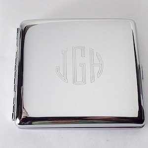 May include: A silver cigarette case with a monogram of the letters "JGH" engraved on the front.