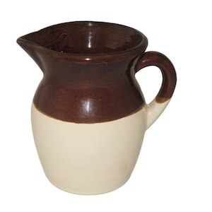 May include: A brown and white ceramic pitcher with a rounded body and a handle. The pitcher is glazed in a brown color on the top half and a white color on the bottom half.