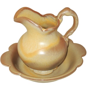 May include: A small, yellow ceramic pitcher with a scalloped rim and a matching saucer. The pitcher has a brown glaze and a slightly textured surface.