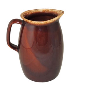 May include: A brown ceramic pitcher with a handle and a spout. The pitcher has a glossy finish and a lighter brown rim. The design is simple and classic, suitable for serving beverages or as a decorative item.