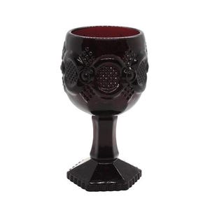 May include: A dark red, vintage-style wine glass. The glass features ornate embossed detailing around the bowl and a hexagonal base. The stem is a solid, dark red color, and the glass is set against a white background.