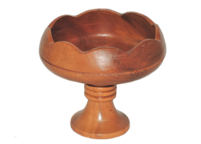 May include: A wooden bowl with a scalloped edge sits on a pedestal base. The bowl is made of light brown wood and has a smooth finish.