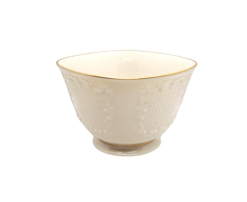 May include: A white porcelain bowl with a gold rim and intricate embossed design. The bowl has a square shape and a rounded bottom.