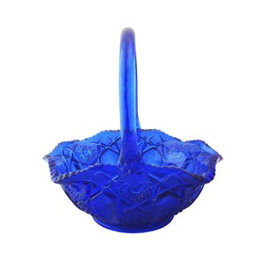 May include: A vibrant cobalt blue glass basket with a handle. The basket features a detailed, textured pattern with a ruffled edge. The handle is arched and smooth, complementing the intricate design of the basket.