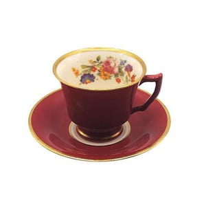 May include: A burgundy teacup and saucer set with gold trim. The inside of the teacup features a floral design with pink, yellow, and blue flowers. The saucer and teacup are a matching burgundy color.