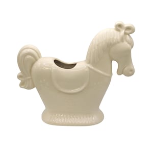 May include: A cream-colored ceramic horse-shaped planter or vessel. The piece features a sculpted mane, a saddle detail on the back, and a small opening at the top. The base has a textured edge, and the body is decorated with subtle floral motifs.