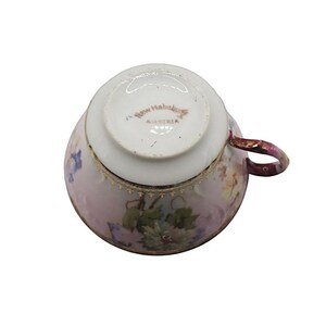 K&ouml;nnte beinhalten: Eine antike Teetasse, von unten betrachtet, mit floralem Muster und Goldverzierungen. Die Tasse ist &uuml;berwiegend rosa mit einem weinroten Henkel. Der Boden ist wei&szlig; und mit "New Hababa Austria" beschriftet.
