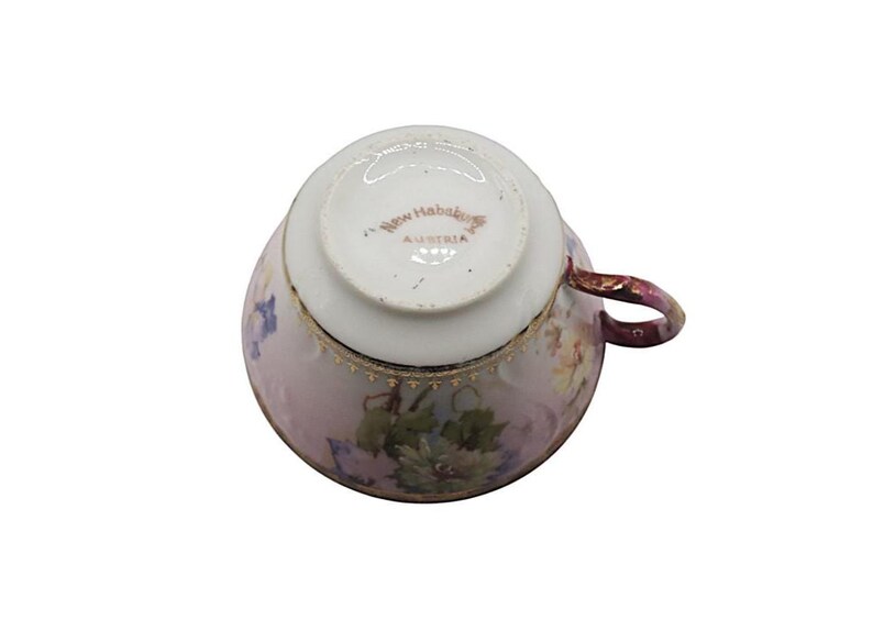 K&ouml;nnte beinhalten: Eine antike Teetasse, von unten betrachtet, mit floralem Muster und Goldverzierungen. Die Tasse ist &uuml;berwiegend rosa mit einem weinroten Henkel. Der Boden ist wei&szlig; und mit "New Hababa Austria" beschriftet.