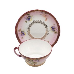 K&ouml;nnte beinhalten: Vintage Tee-Set, bestehend aus Tasse und Untertasse. Die Tasse und Untertasse haben einen rosa-wei&szlig;en Hintergrund mit floralen und goldenen Akzenten. Der Rand der Tasse und Untertasse ist goldfarben.