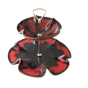 May include: Two-tiered serving stand with a gold metal handle. The stand is made of ceramic and features a black and red floral design.