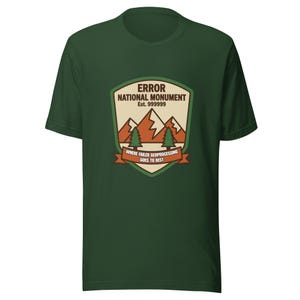 May include: A dark green t-shirt featuring a graphic of a national park badge. The badge includes the text "ERROR NATIONAL MONUMENT" and "WHERE FAILED GEOPROCESSING GOES TO REST". The design incorporates mountains, trees, and a banner.