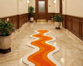 Puede incluir: Una alfombra ondulada de color naranja, blanco y crema en un pasillo. El diseño de la alfombra se asemeja a un río que fluye. El pasillo tiene suelo de mármol, paneles de madera y plantas en macetas. La alfombra añade un toque de color al espacio neutro.