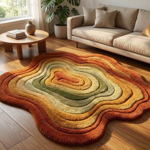 May include: A multi-coloured rug with a layered design. The rug features a gradient of warm colours, including shades of orange, yellow, and green. The rug is placed on a wooden floor, and the design resembles a topographical map.