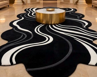 Peut inclure: Un grand tapis de forme irrégulière présentant un fond noir avec des motifs ondulés fluides en blanc et gris. Le tapis est placé sur un sol poli sous une table basse ronde avec un plateau en marbre blanc et une base dorée.