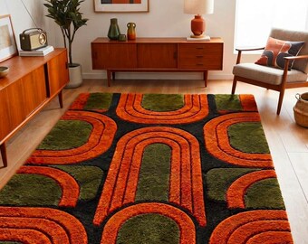 May include: A rectangular area rug featuring a repeating geometric pattern of bold, raised orange arches set against a deep black background with interspersed dark olive green sections, creating a textured, high-pile surface design.