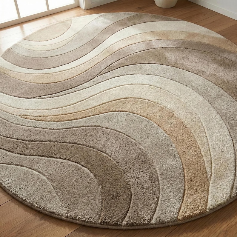 May include: A round rug with a wave pattern in shades of beige, tan, and brown. The rug has a soft, plush texture and is designed with a flowing, curved pattern. The rug is placed on a wooden floor.