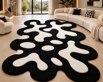 May include: An area rug with an irregular, organic shape featuring a high-contrast pattern of large, flowing white blobs and spots set against a solid black background. The rug has a soft, textured pile and curved, rounded edges throughout its design.