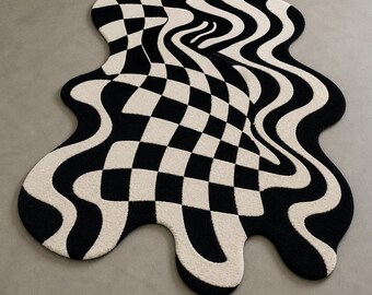 May include: An irregularly shaped area rug featuring a high-contrast black and white pattern. The design transitions from a structured checkerboard grid on one side into fluid, wavy, and distorted lines that create a sense of motion across the surface.