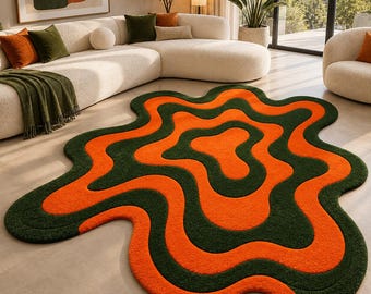 Peut inclure: Un tapis de forme organique irrégulière présentant un motif ondulé répétitif composé de bandes concentriques orange vif et vert forêt profond. Le tapis possède une surface texturée et moelleuse, posé à plat sur un sol clair.