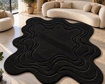 May include: A large, solid black area rug with an irregular, organic shape. The rug features a series of concentric, wavy, carved-out channels that follow the perimeter, creating a layered, topographical effect across the entire surface.