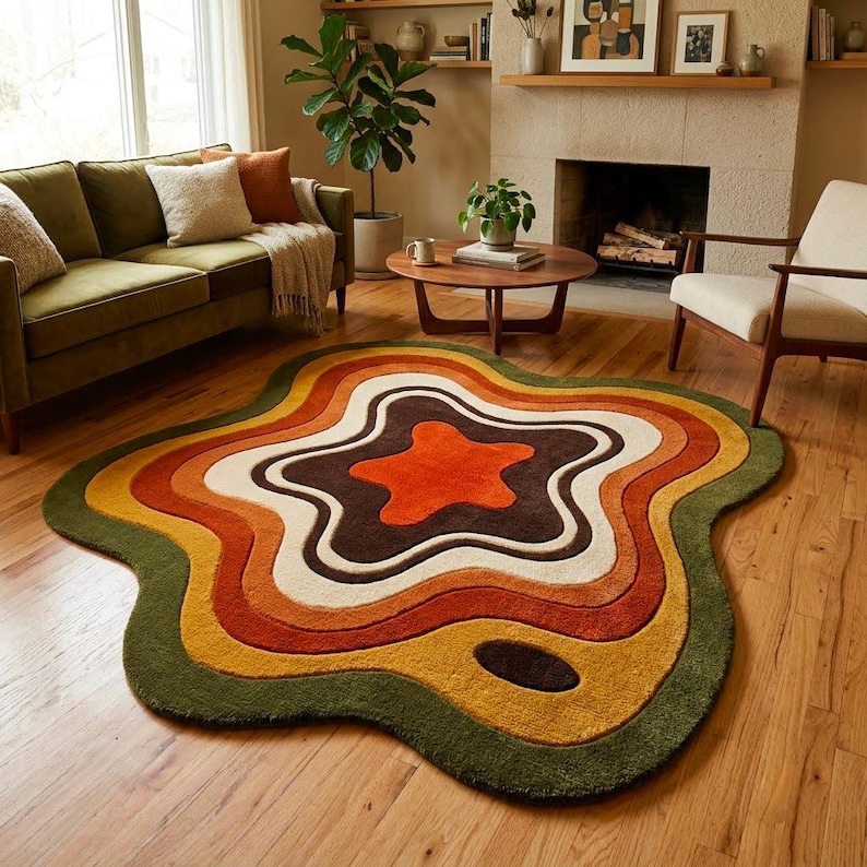 Puede incluir: Una alfombra de forma org&aacute;nica irregular con bandas conc&eacute;ntricas onduladas en colores verde oliva oscuro, amarillo mostaza, naranja quemado, crema y marr&oacute;n oscuro. La alfombra tiene un pelo texturizado y denso sobre un suelo de madera clara.