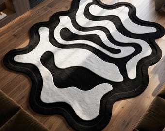 Puede incluir: Una alfombra con una forma orgánica irregular que presenta un patrón de alto contraste de bandas negras y blancas onduladas y fluidas. El diseño consiste en líneas curvas superpuestas que crean una estética abstracta en toda la superficie.
