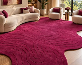 May include: A large, deep magenta area rug with an irregular, organic shape and a textured surface featuring carved, flowing wave patterns that create a sense of movement across the floor. The rug has a thick, plush pile and a solid, vibrant color.